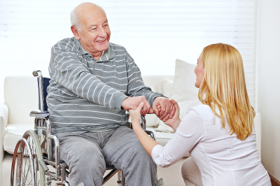 woman holding hands of old man in wheelchair