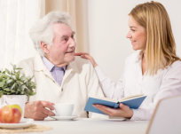 elderly man having a cup of tea while talking from a caregiver